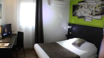A hotel room with a bed, a desk with a chair, a television, and a wall-mounted air conditioner.