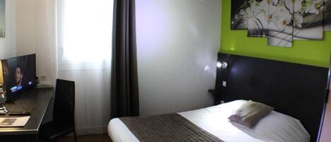 Una habitación de hotel con una cama, un escritorio con una silla, un televisor y un aire acondicionado instalado en la pared.