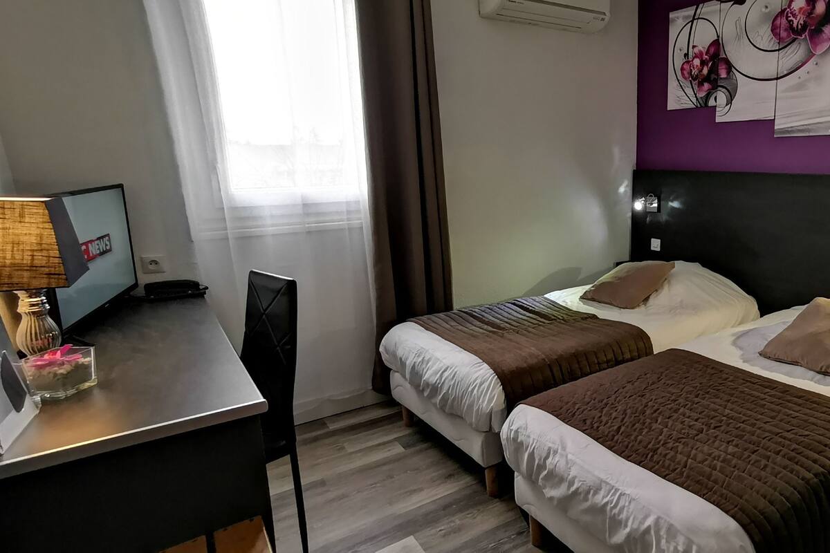A hotel room with two beds, a desk with a lamp, and a wall with a floral painting.