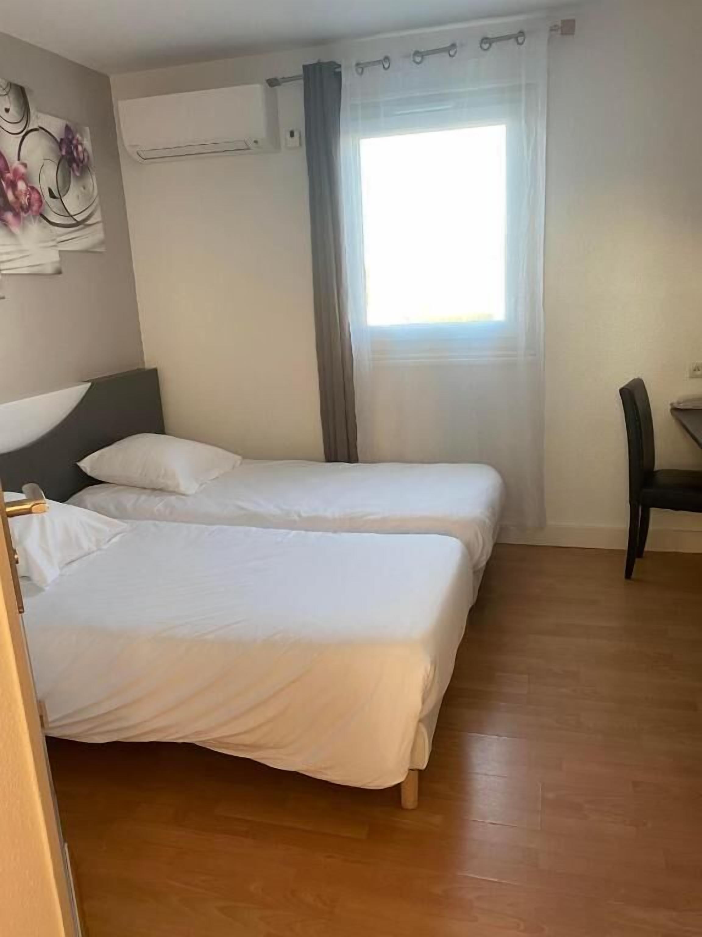 Quarto de hotel com duas camas, uma escrivaninha e uma cadeira.