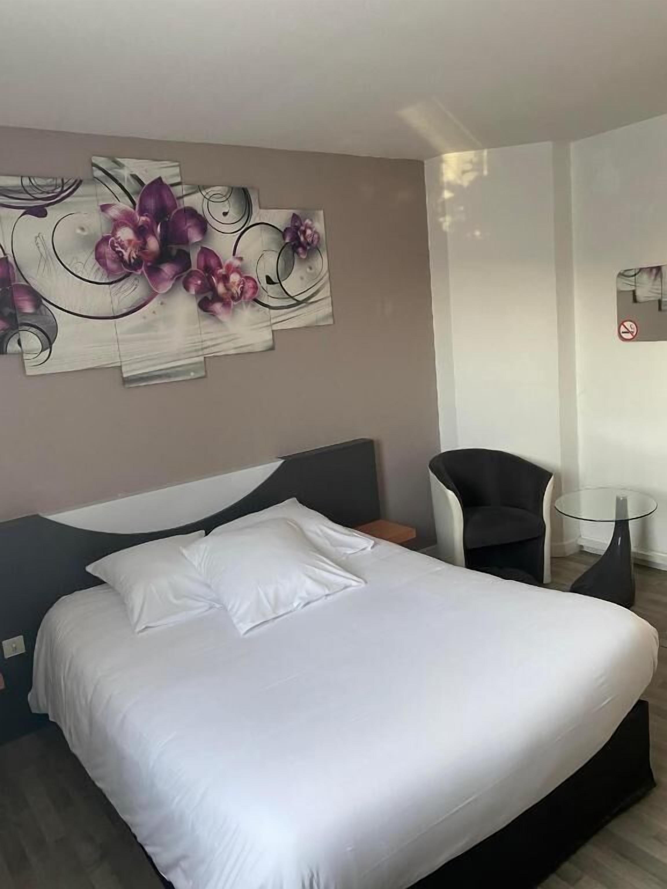 A hotel room with a large bed, a chair, a small table, and a wall art piece.