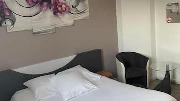 A hotel room with a large bed, a chair, a small table, and a wall art piece.