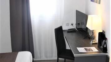 Una habitación de hotel con cama, escritorio, silla, lámpara y una mesita.