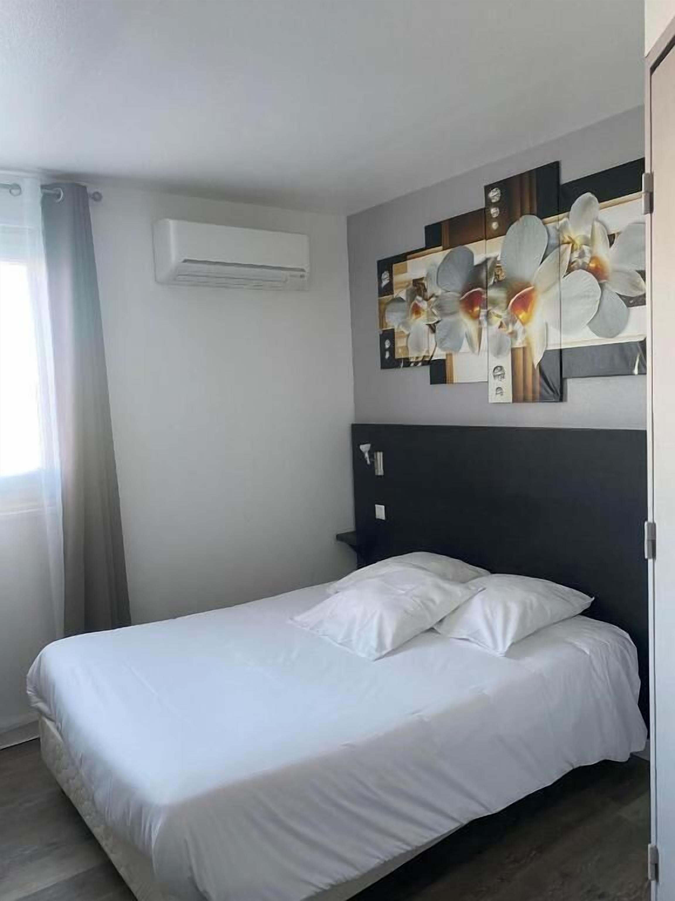 A single bed with white bedding in a room with a dark headboard and a wall-mounted air conditioning unit.