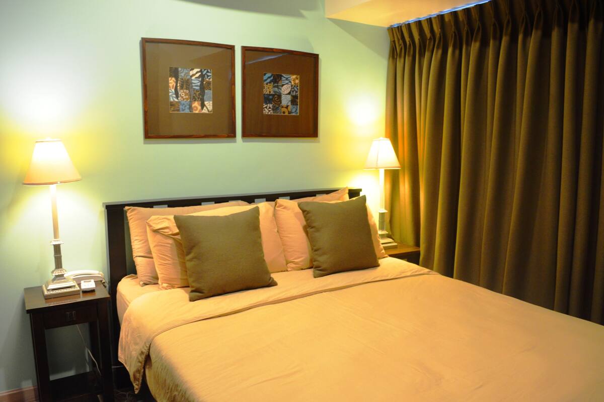 Une chambre d’hôtel avec un lit, deux lampes de chevet, une table de chevet et deux tableaux encadrés au mur.