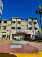 Hotel com uma placa indicando "Poco de Playa Hotel" e uma entrada ampla com área pavimentada na frente.