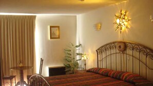 A bedroom with a bed, a chair, a table, and a plant. - Hotel Pueblito Inn (Playas de Rosarito)