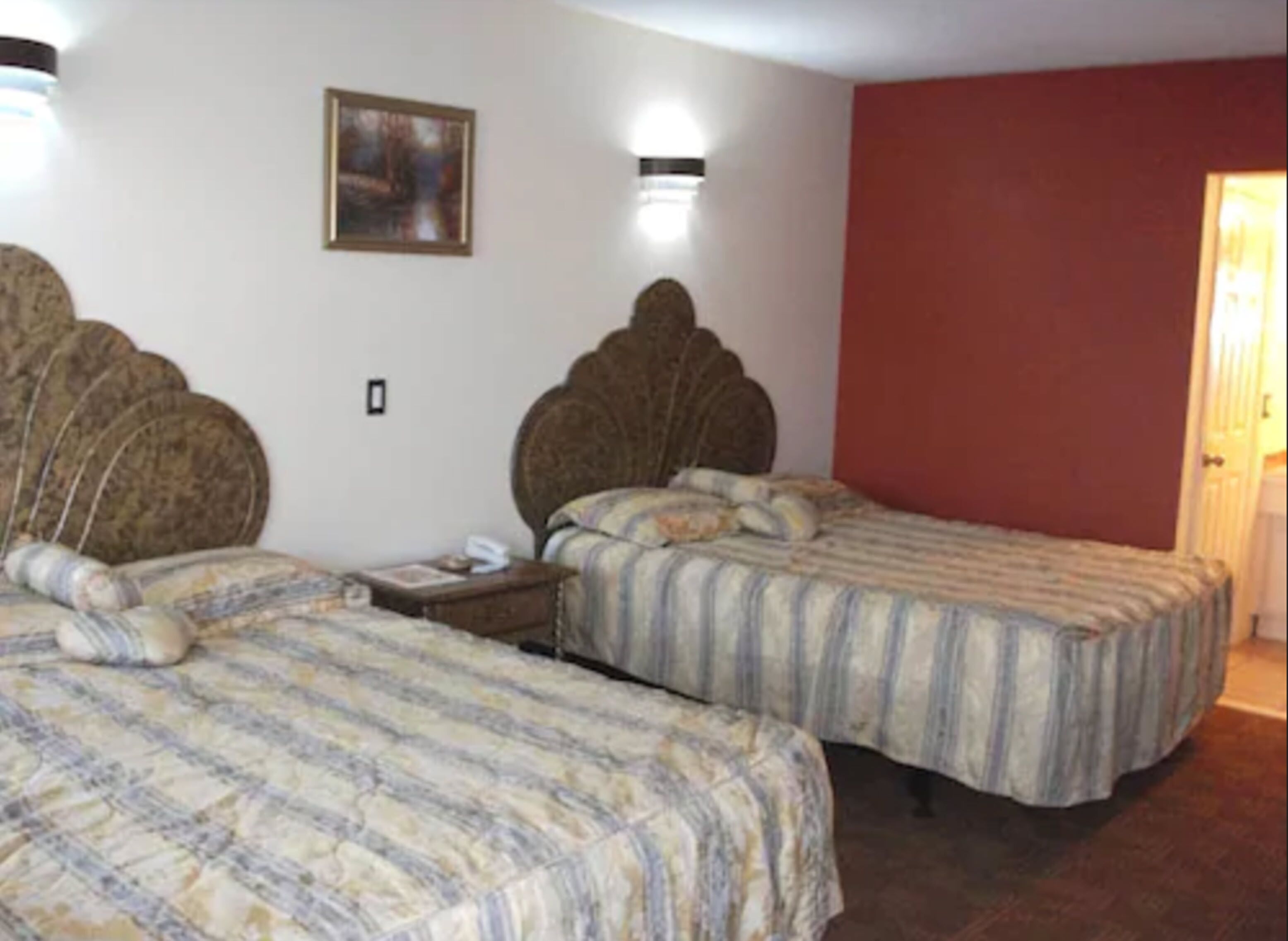Una habitación con dos camas, cada una con cabecera y colcha a rayas. Hay un cuadro en la pared y una mesita de noche con una lámpara entre las camas.