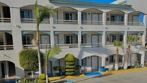 A multi-story hotel with a courtyard featuring landscaped gardens and palm trees. - Hotel Pueblito Inn (Playas de Rosarito)