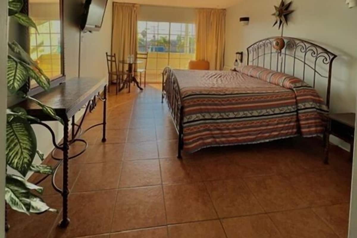 A bedroom with a bed, a desk, a chair, a TV, and a window with curtains.
