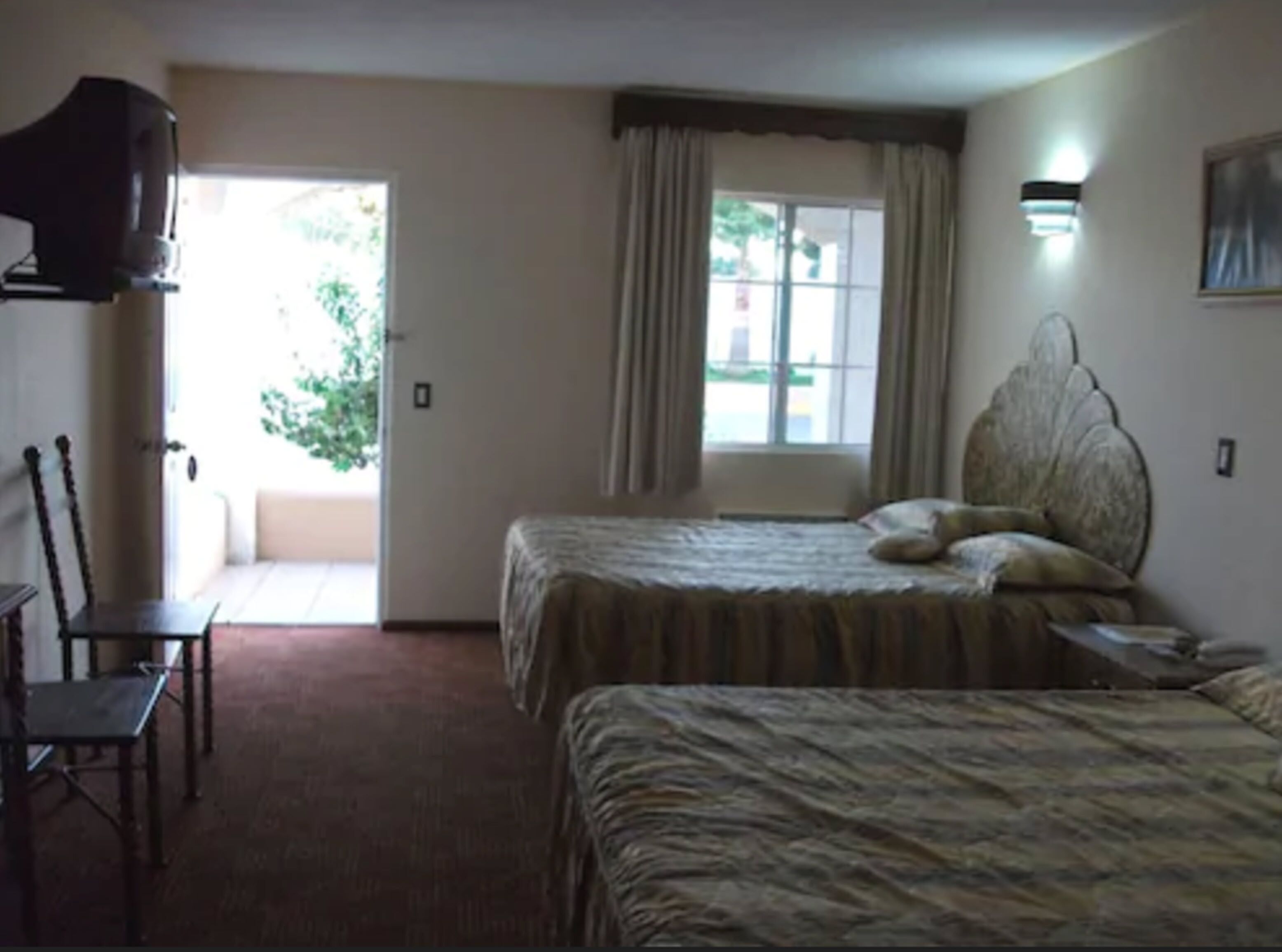A hotel room with two beds, a chair, a television, and a window with curtains.
