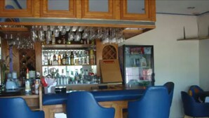 A bar area with wooden cabinets, blue bar stools, and a variety of bottles and glasses on shelves. - Hotel Pueblito Inn (Playas de Rosarito)