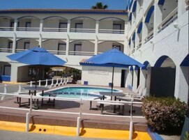 A hotel with a pool area, multiple balconies, and blue umbrellas.