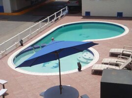 A swimming pool with lounge chairs and a blue umbrella.