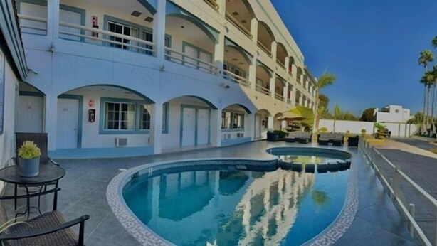 A hotel with a swimming pool, outdoor seating, and a multi-story building with balconies. - Hotel Pueblito Inn (Playas de Rosarito)
