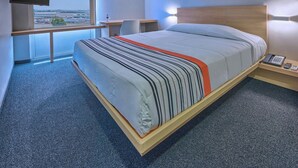 A hotel room with a bed, a desk, a chair, a TV, and a view of an airport. - City Express Junior by Marriott Guadalajara Periférico Sur (Tlaquepaque)
