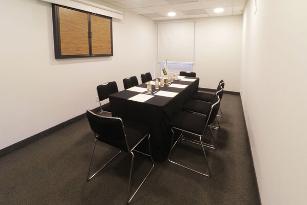 Un salón de conferencias con una larga mesa, sillas negras y botellas de agua sobre la mesa.