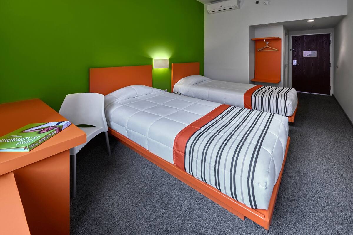 Ein Hotelzimmer mit zwei Betten, einem Schreibtisch, einem Stuhl und einer grünen Wand.