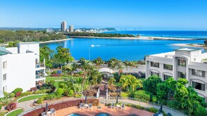A resort with a swimming pool, palm trees, and a view of the ocean and city skyline.