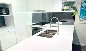 A modern kitchen with white cabinetry, a stainless steel sink, and a black microwave. - Little Cove Currumbin (Currumbin)