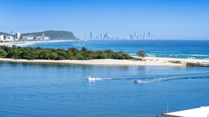A coastal cityscape with a beach, a boat, and a person wakeboarding.