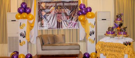 A room with a sofa, a table with a cake, and balloons.