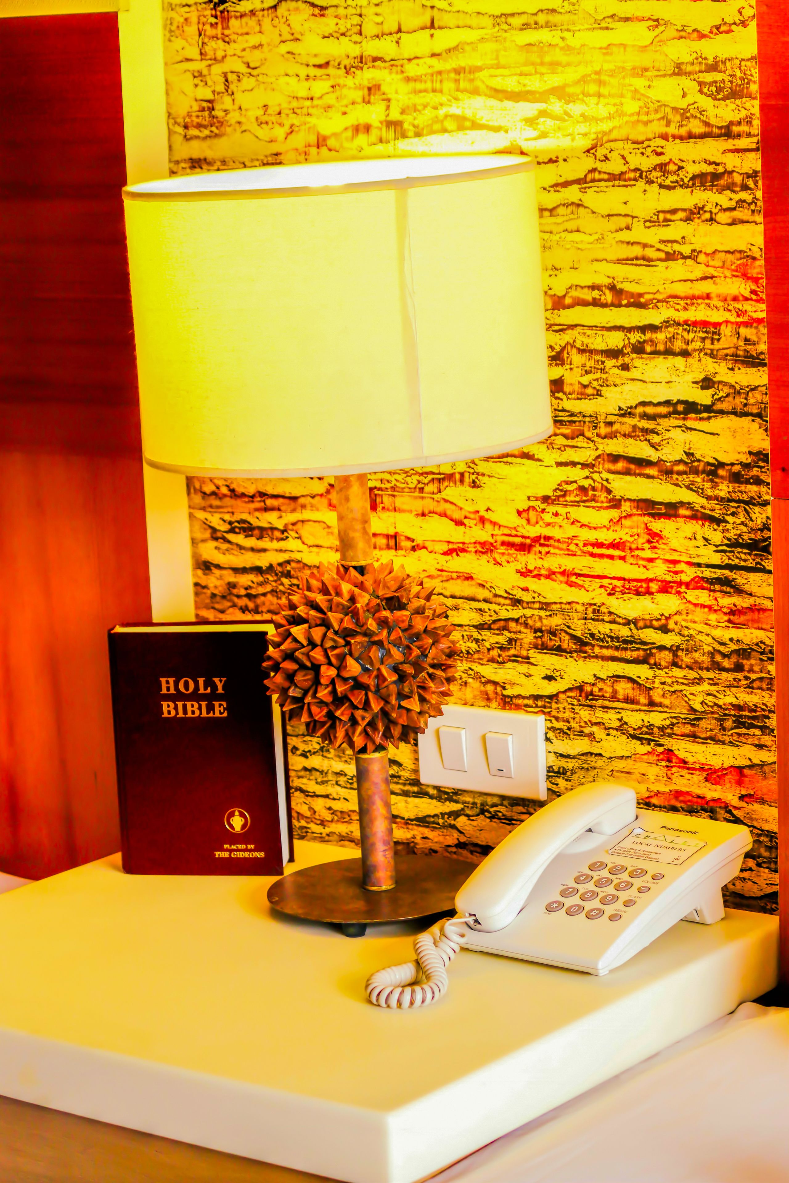 Una mesita de noche con una Biblia, una lámpara y un teléfono.