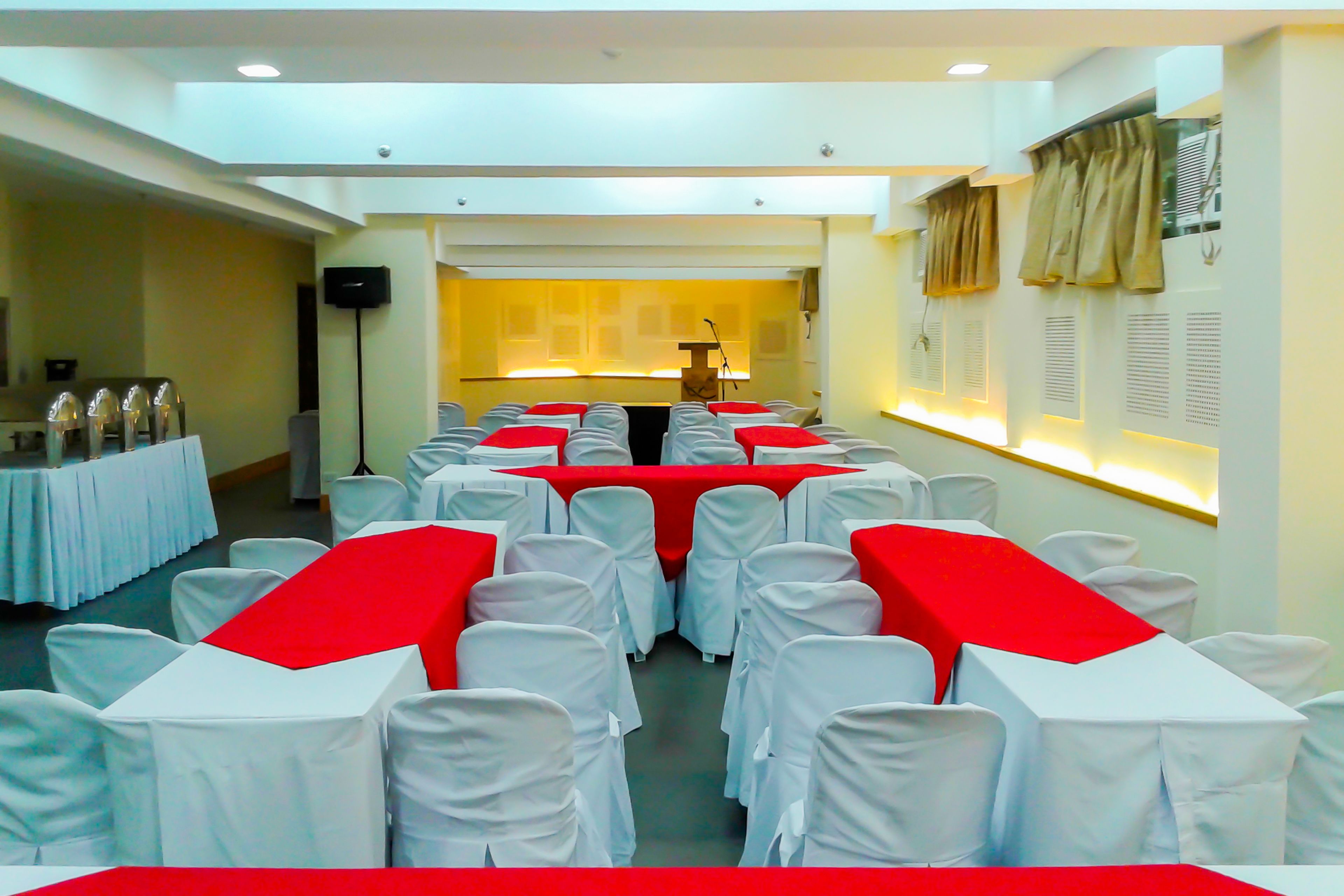 Un salón de conferencias con filas de sillas blancas, manteles rojos y un atril al frente.