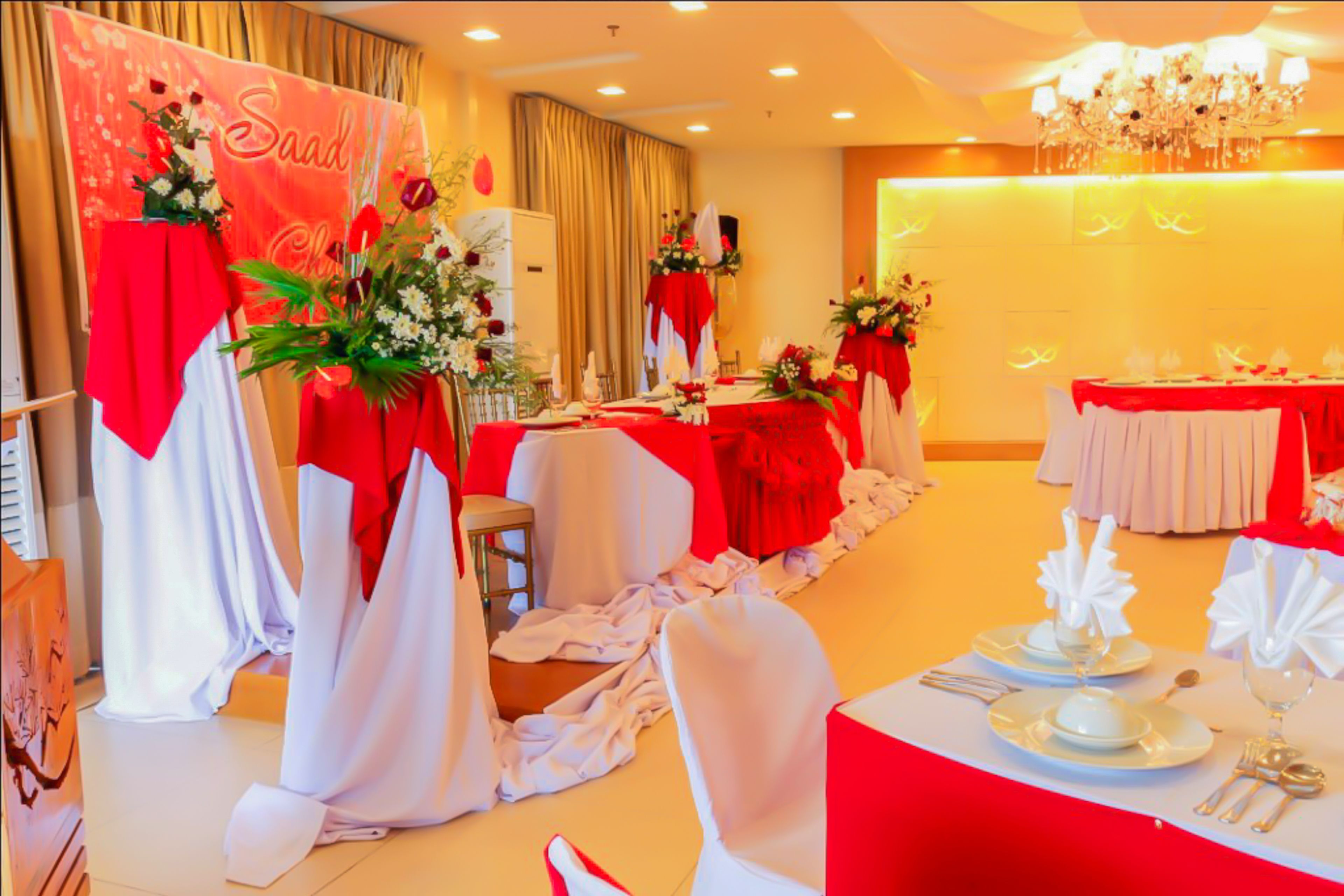 A banquet hall with tables set for a formal event, featuring red and white tablecloths and floral centerpieces.