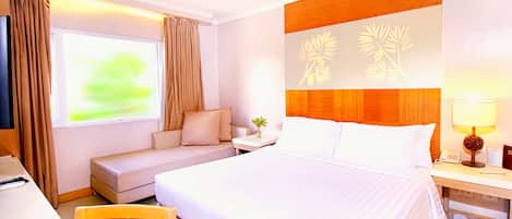 Una habitación de hotel con una cama grande, un sofá, un escritorio y una mesita de noche con una lámpara.