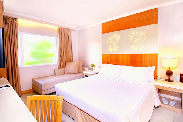 A hotel room with a large bed, a sofa, a desk, and a nightstand with a lamp. - Chalet Baguio (Baguio)