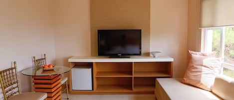 A compact living space with a television on a stand, a dining table with chairs, a sofa, and a window.