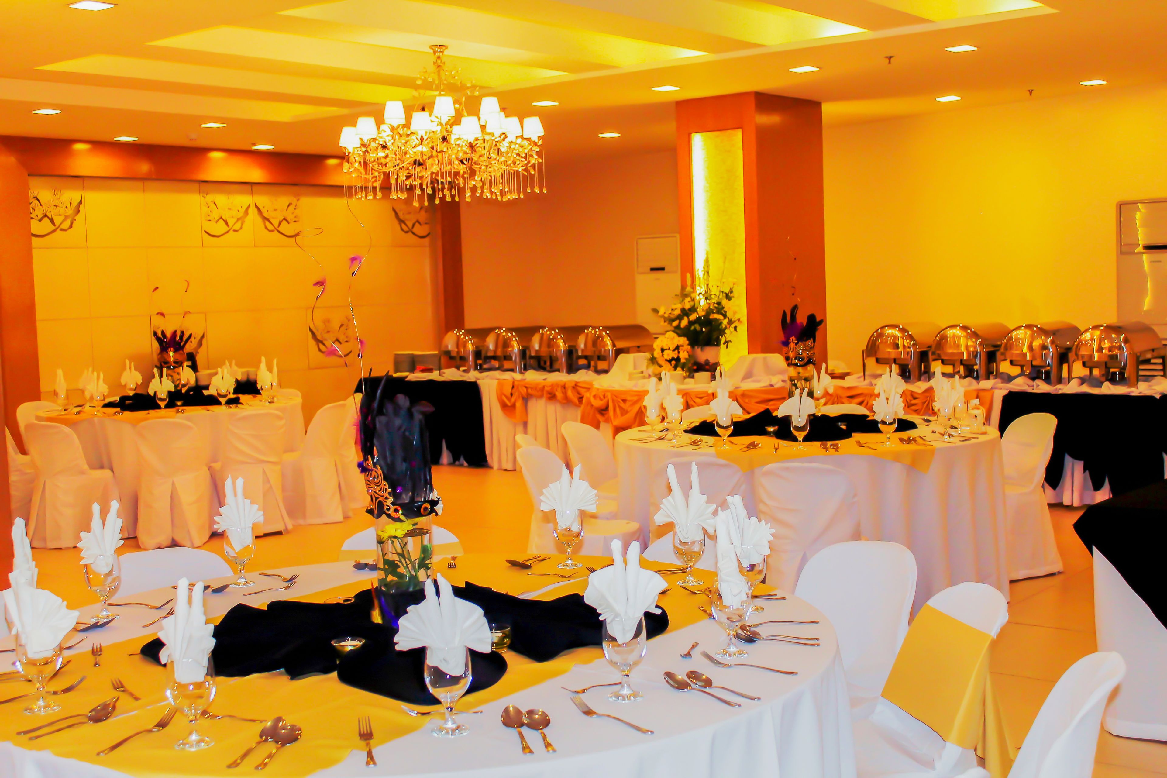 A banquet hall with round tables set for a formal event, featuring white tablecloths, gold accents, and a chandelier.