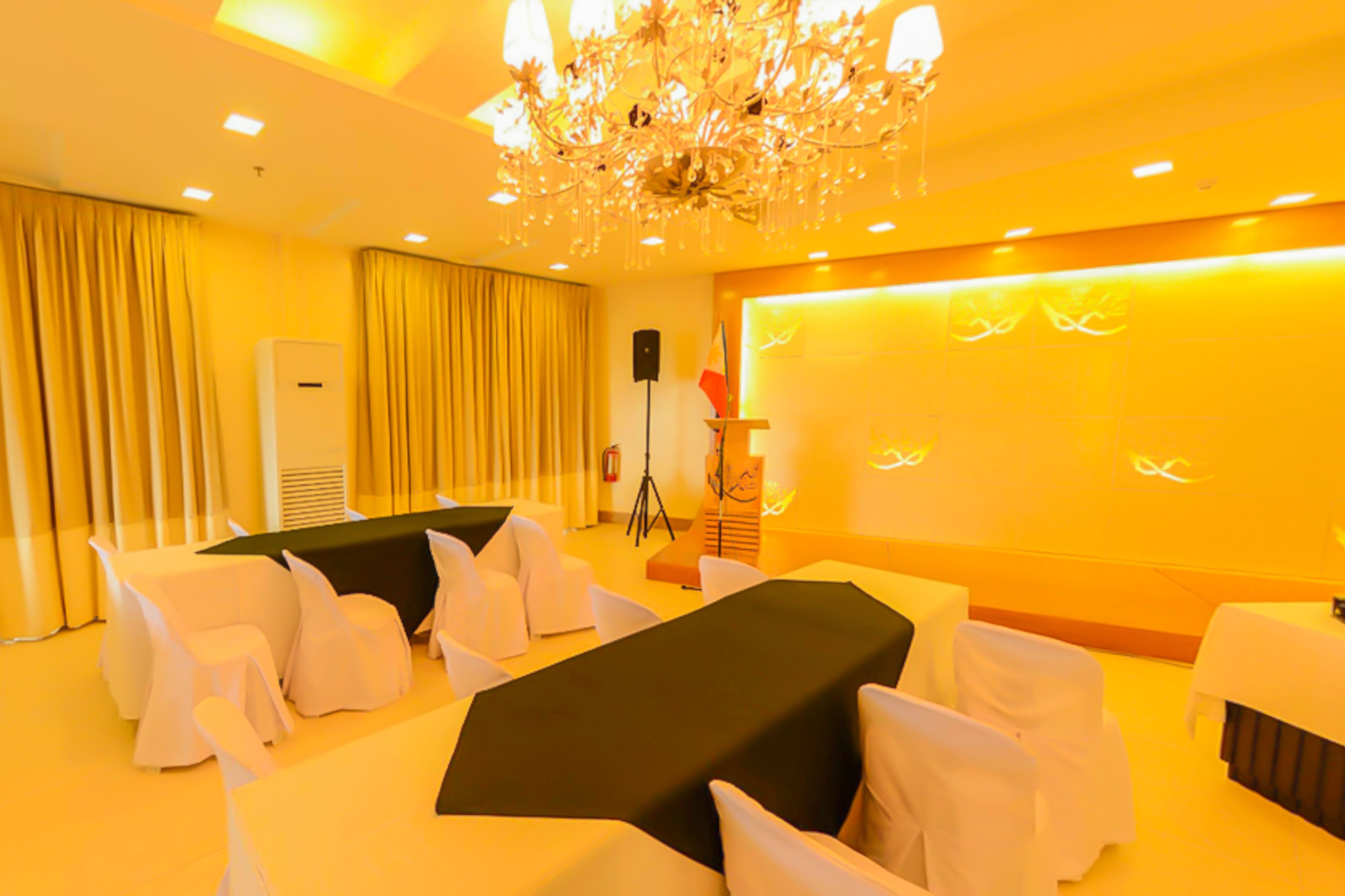 A conference room with a long table, white chairs, a chandelier, and a speaker.