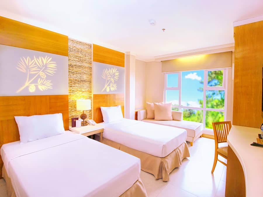 A hotel room with two beds, a desk, a TV, and a window with a view of greenery.