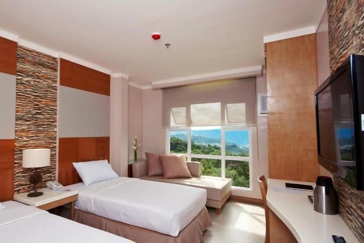 A hotel room with two beds, a desk, a TV, and a large window with a view.