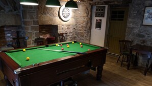 A pool table with balls, a dartboard, and a clock on a stone wall. - The Commercial Hotel (Aboyne)
