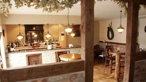 A bar area with a brick wall, wooden furniture, and hanging pendant lights. - The Commercial Hotel (Aboyne)