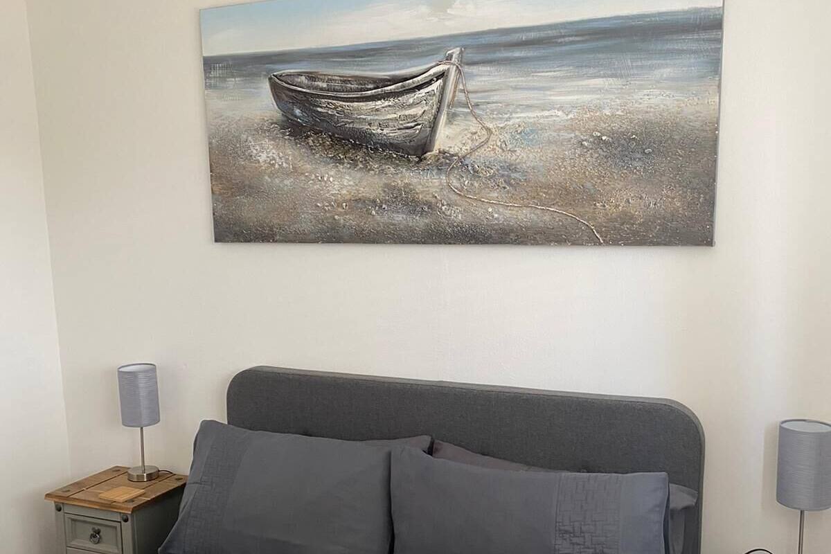 Une chambre à coucher avec un lit, deux tables de chevet et un tableau représentant un bateau accroché au mur.
