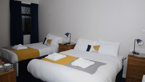 Ein Hotelzimmer mit zwei Betten, einem Nachttisch aus Holz mit Lampe, einem kleinen Tisch ebenfalls mit Lampe und einem Fenster mit Vorhängen.