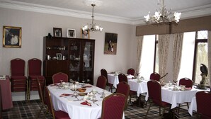 Ein Esszimmer mit mehreren gedeckten Tischen, rot gepolsterten Stühlen, einer Holzkabine mit Glastüren und einem Kronleuchter.