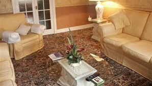 Ein Wohnzimmer mit zwei beigefarbenen Sofas, einem gemusterten Teppich, einem kleinen Tisch mit Lampe und einer Glastür.