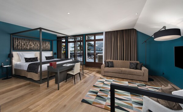 A modern hotel room with a large bed, a sofa, a dining table, and a view of the outdoors. - Auberge Du Père Bise (Talloires-Montmin)