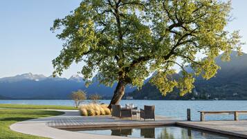 Eine Terrasse am Seeufer mit einer Bank, Liegestühlen und einem kleinen Tisch.