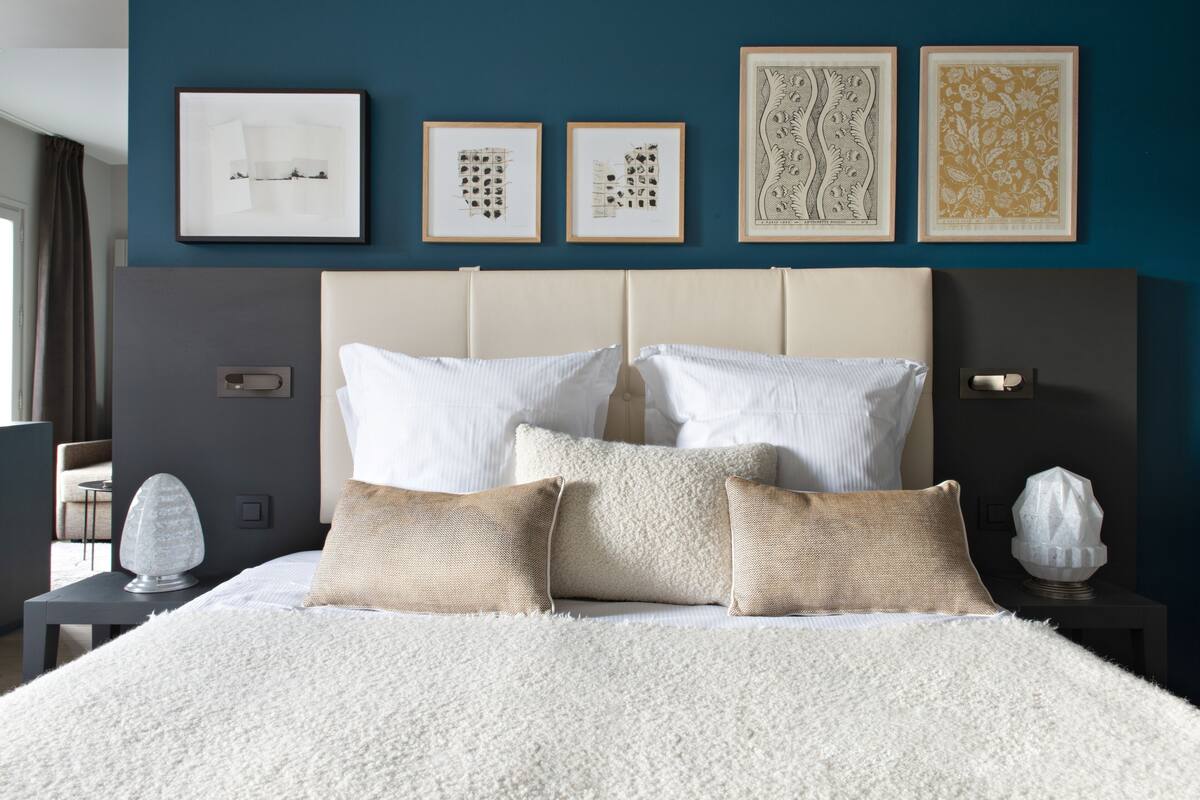 Een slaapkamer met een groot bed, meerdere kussens, een hoofdbord en lijstwerken aan de muur.