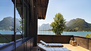 Une terrasse en bois avec deux chaises longues et une table, offrant une vue sur un lac et des montagnes.