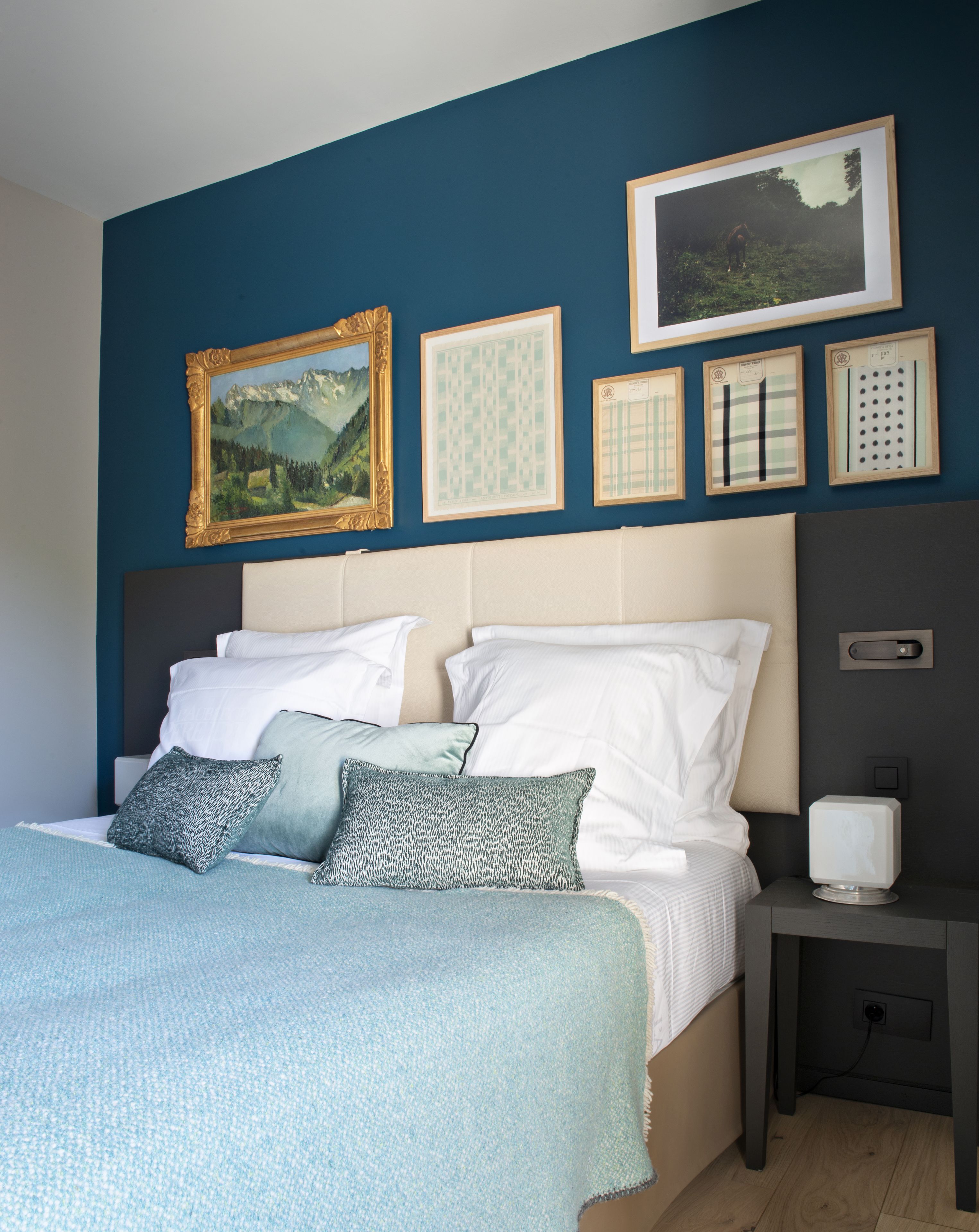 Un dormitorio con cama, almohadas, mesita de noche y cuadros en la pared.