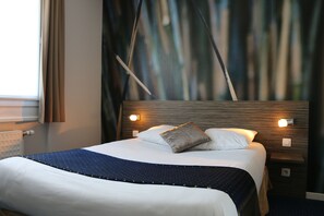 Una cama bien tendida con una manta azul, dos almohadas y un cabecero de madera con luces fijadas a la pared.