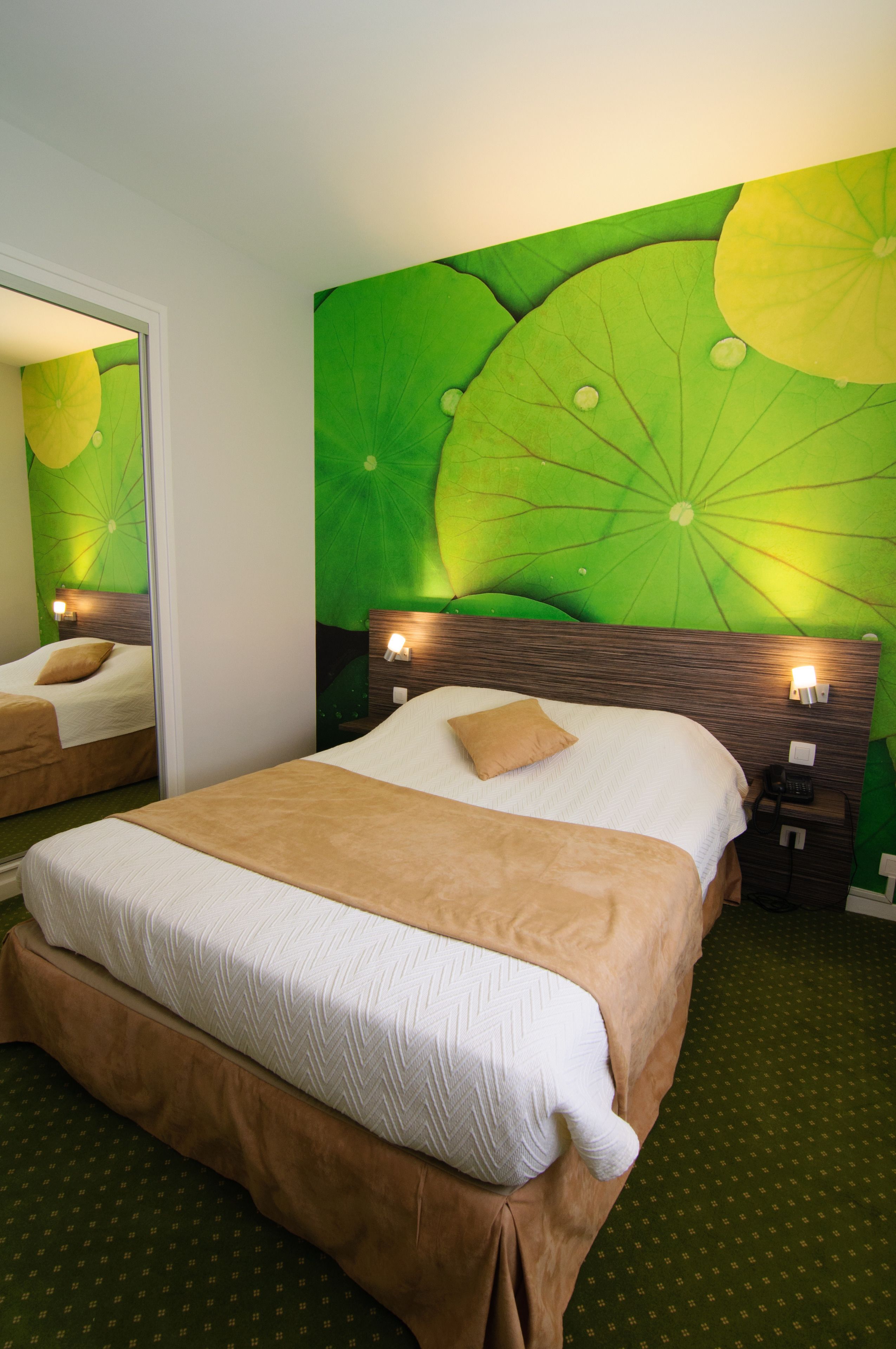 Een hotelkamer met een groot bed, twee nachtkastjes met lampen, een spiegel, en een muurschildering van een groen blad.