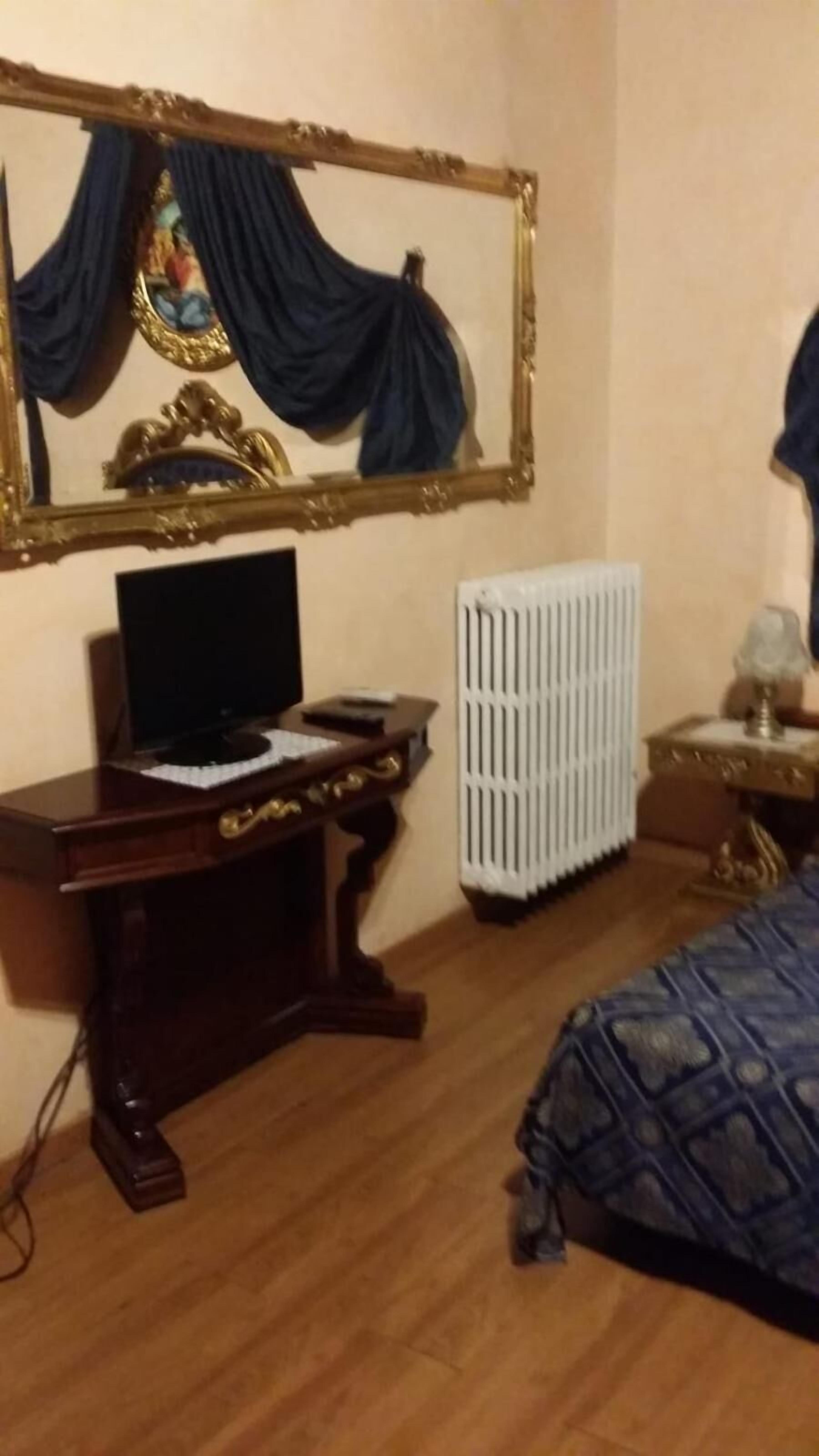 Een slaapkamer met een houten bureau, een computer, een radiator en een bed met een bedekker met een patroon.